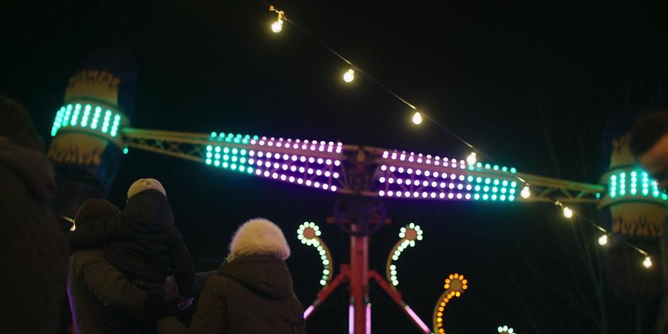 Luke holds Hannah in his arms while they look up at a ride with June.