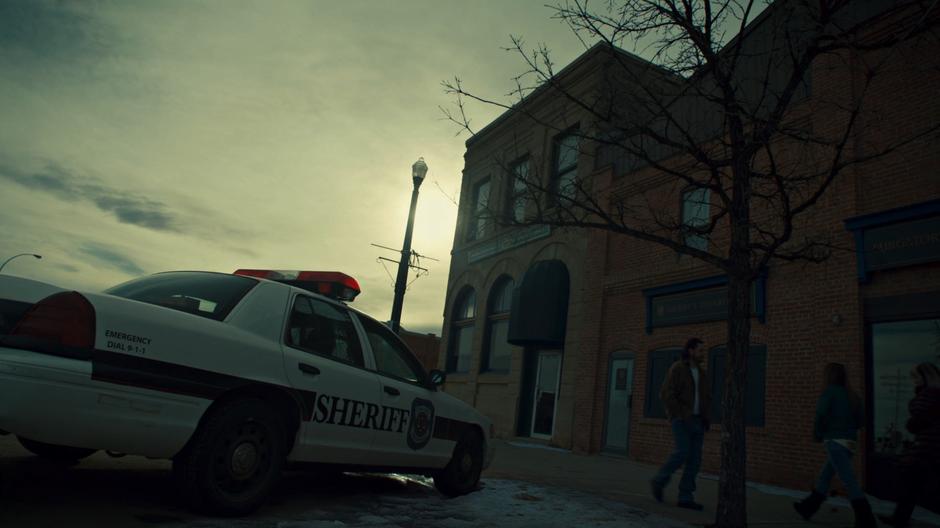 Establishing shot of the front of the building with a police car parked out front.
