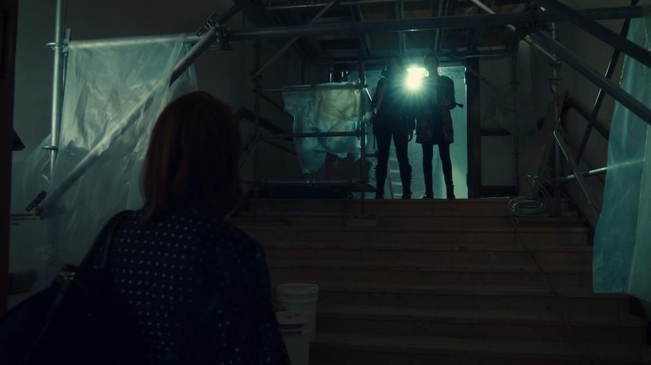 Mercedes looks up the stairs to where Wynonna and Waverly are standing covered in goo.