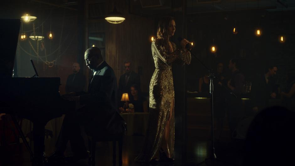 Waverly stands at the microphone in a stunning dress next a to a piano player and gets ready to sing her song.
