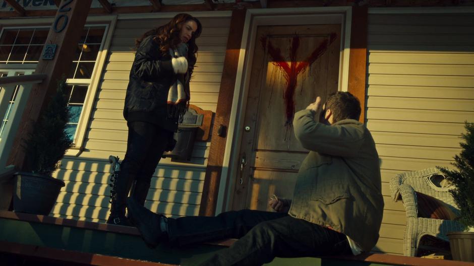 Wynonna looks down at Skip on the ground while a marking in blood decorates the front door.