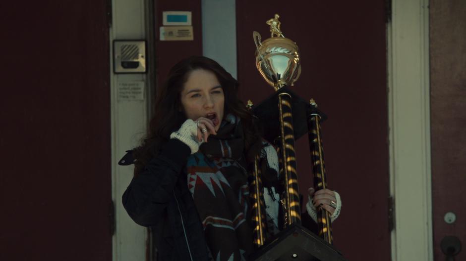 Wynonna wipes some blood from her lip while carrying the newly stolen trophy from the arena.