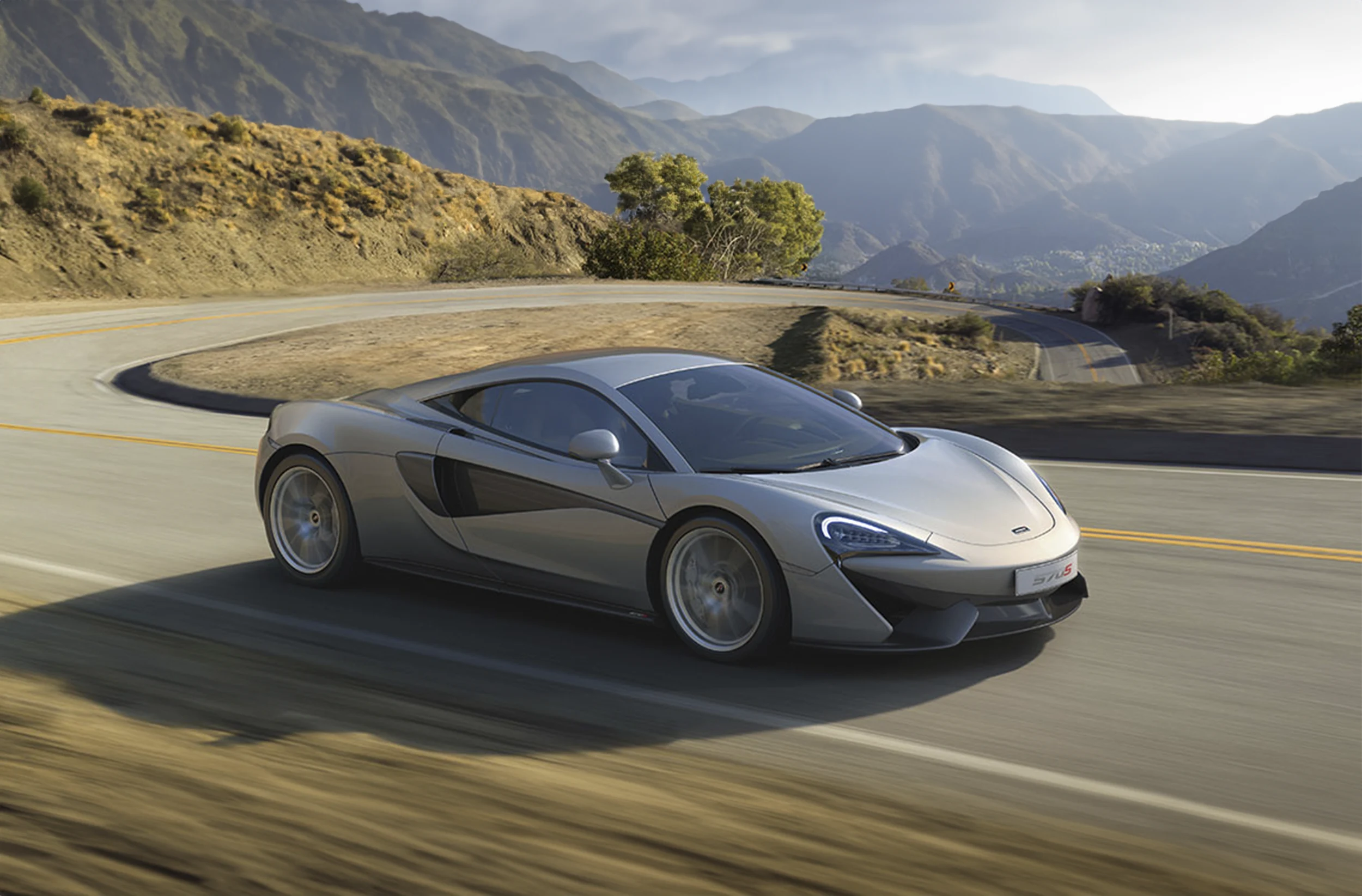 Silver McLaren 570s driving down the road through the mountains