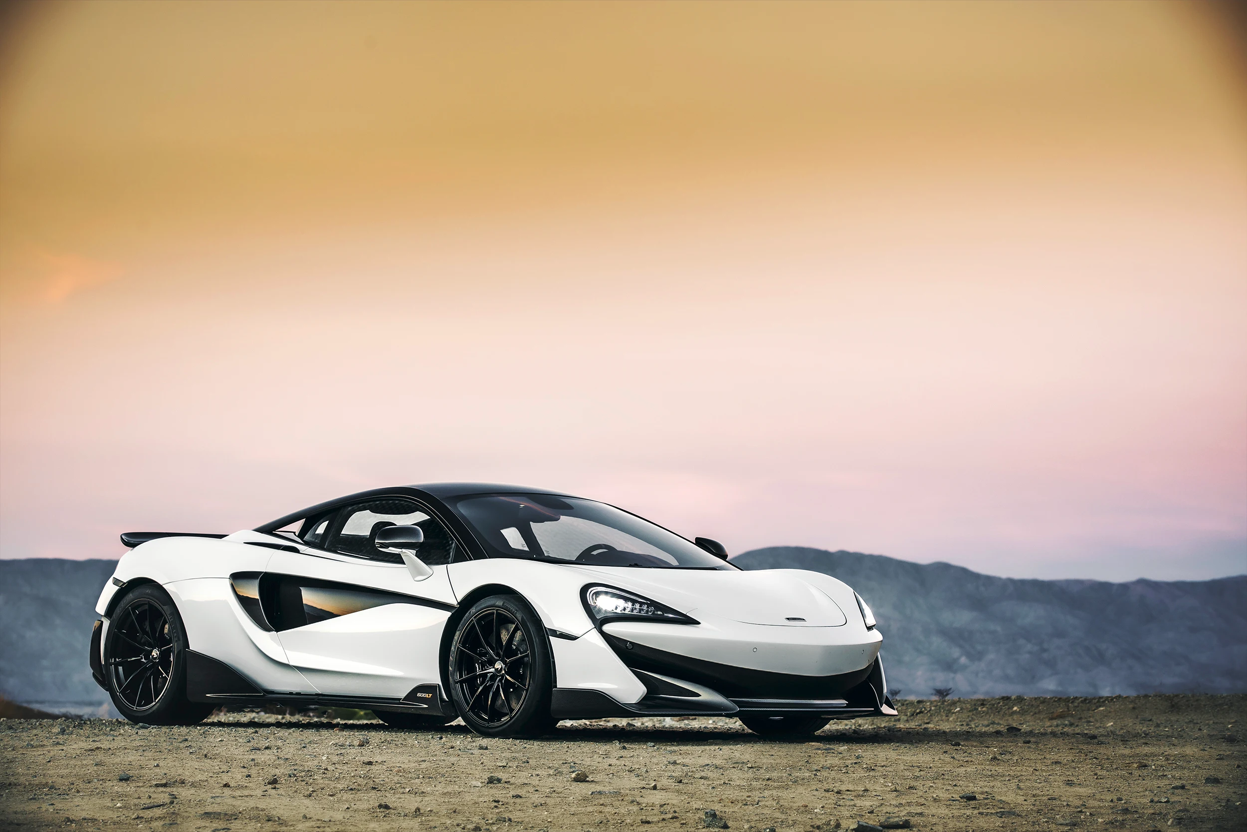 McLaren Boston 600LT White 600LT parked on dirt in front of mountains during sunset.
