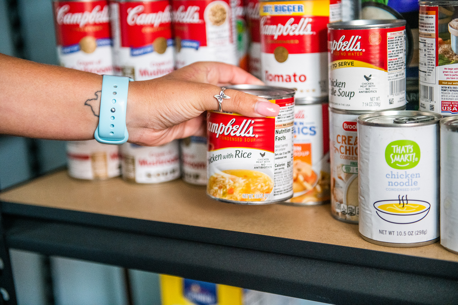 An individual grabbing a can of food from a shelf. 