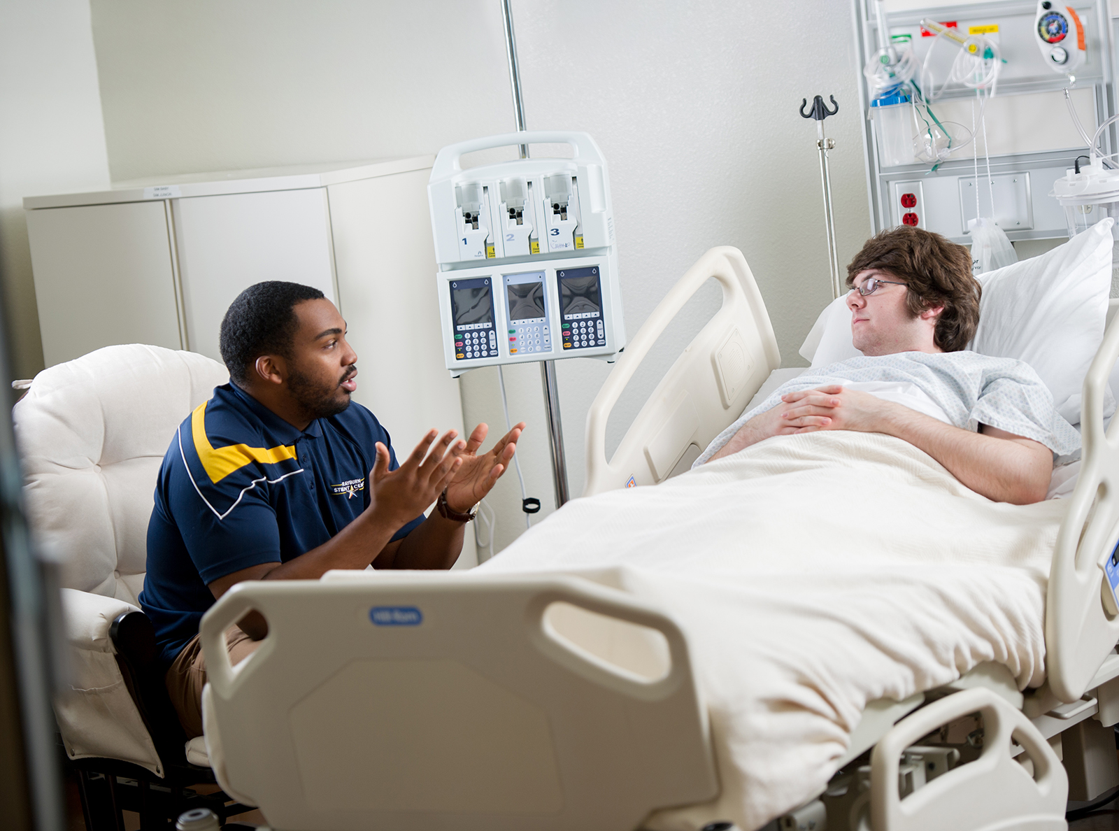 A student laydown in a hospital bed listening to a counselor.