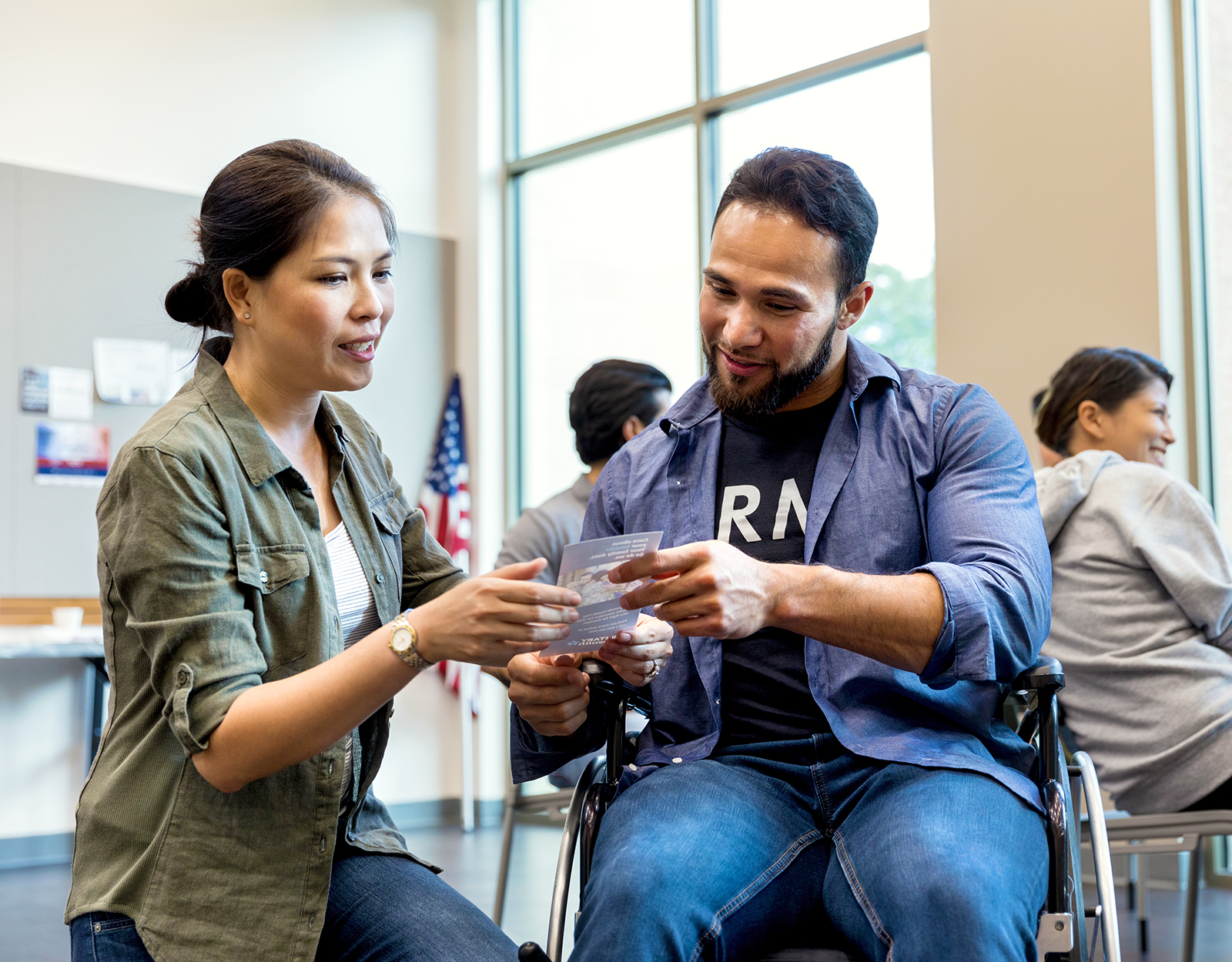 A male in a wheelchair showing a poster card to a female.