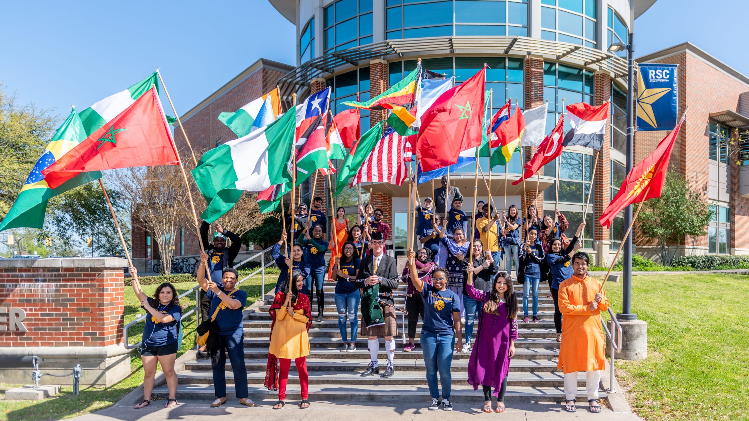 学生 outside the Rayburn Student Center waving multiple distinct national flags.