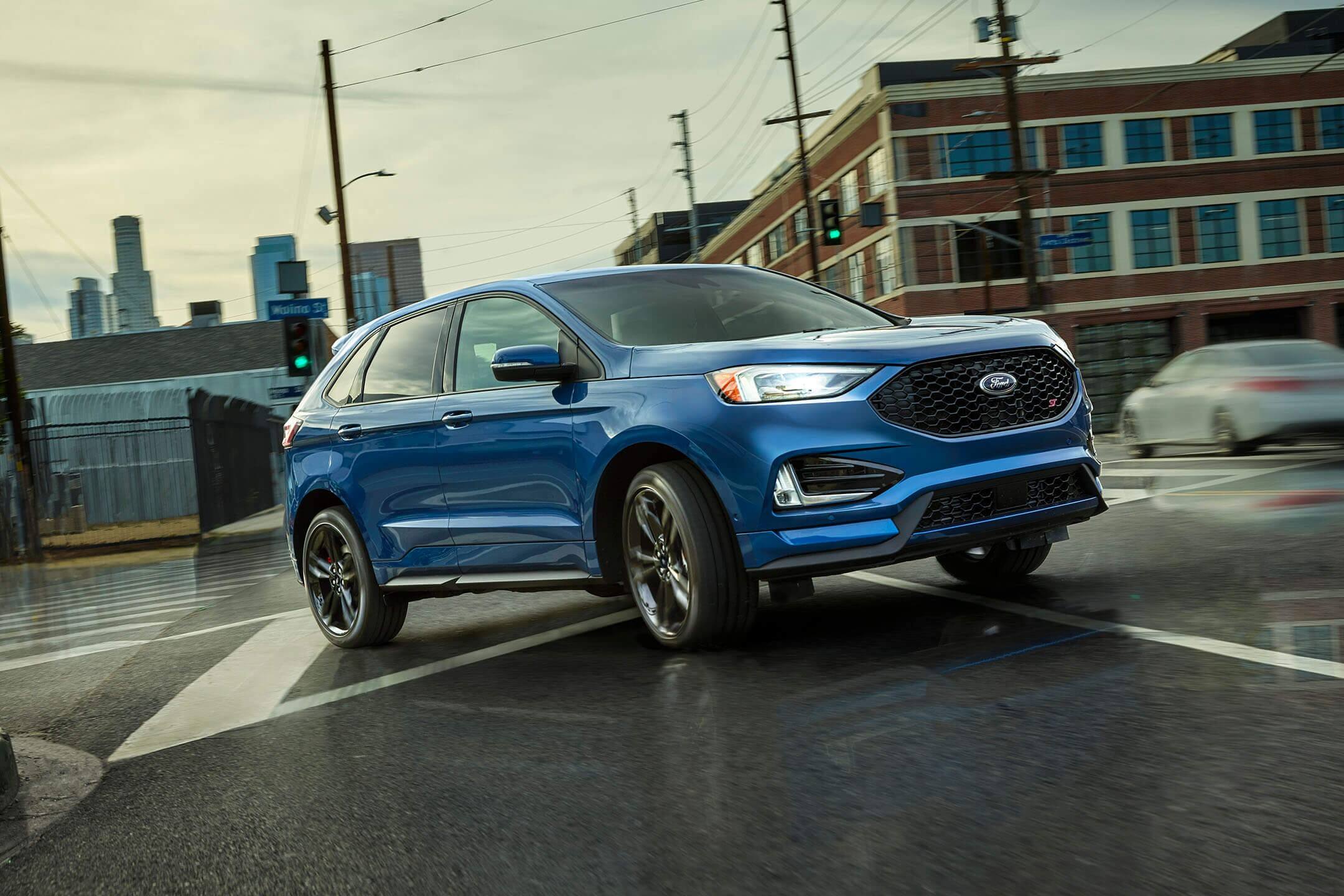 blue 2019 ford edge st driving on a wet city street