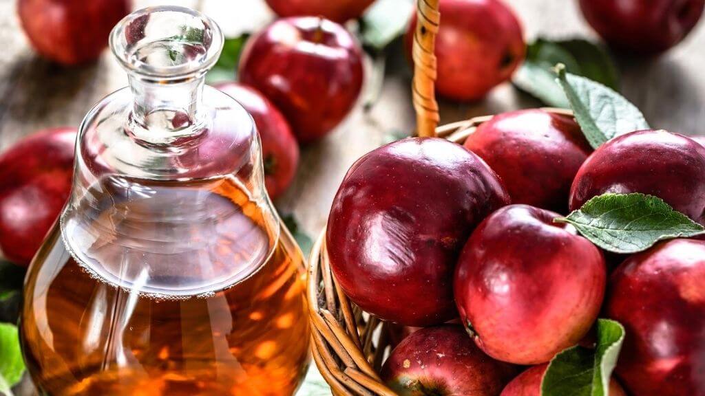 a bottle of apple cider vinegar next to a basket of red apples