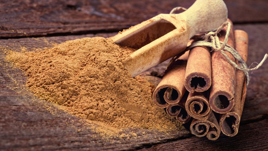 Cinnamon sticks tied with a string and cinnamon powder on and spilling around a wooden spoon.