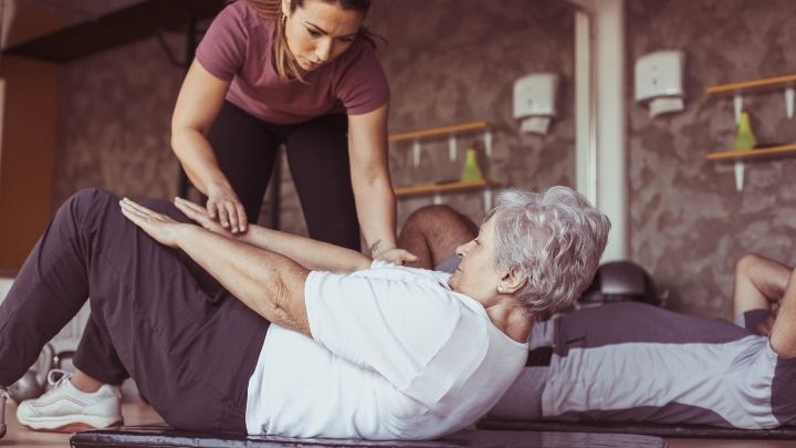 A trainer helps an older woman work out in the gym