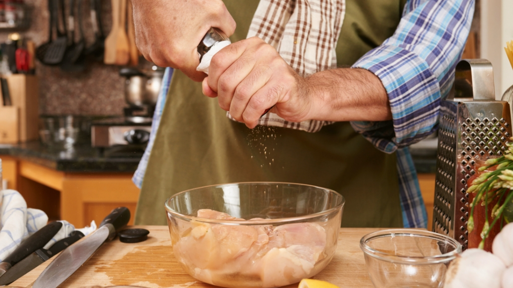 Man putting pepper on raw chicken in the kitchen