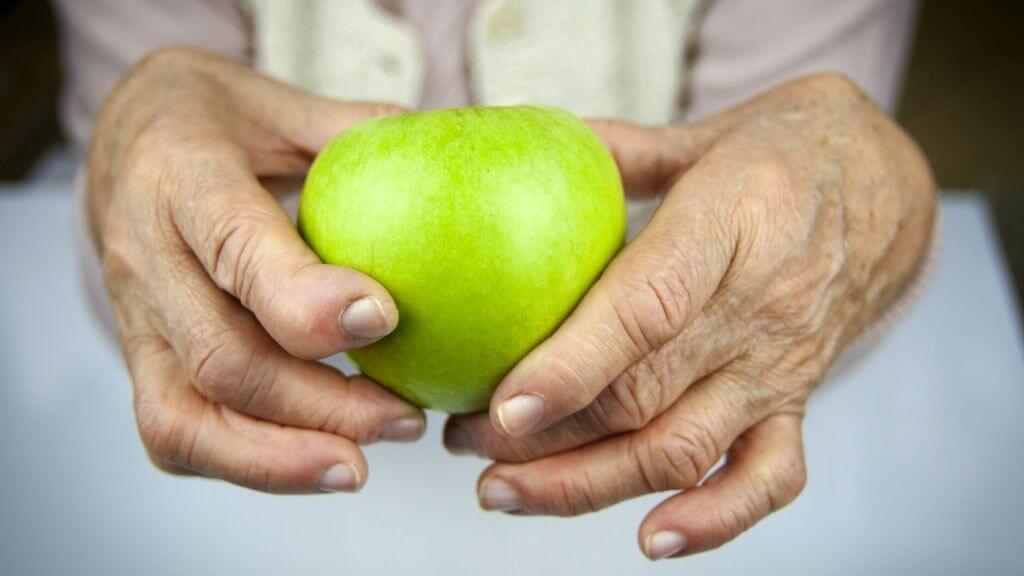 Hands with arthritis holding a green apple