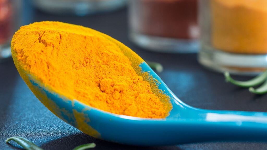 Turmeric powder in a blue spoon