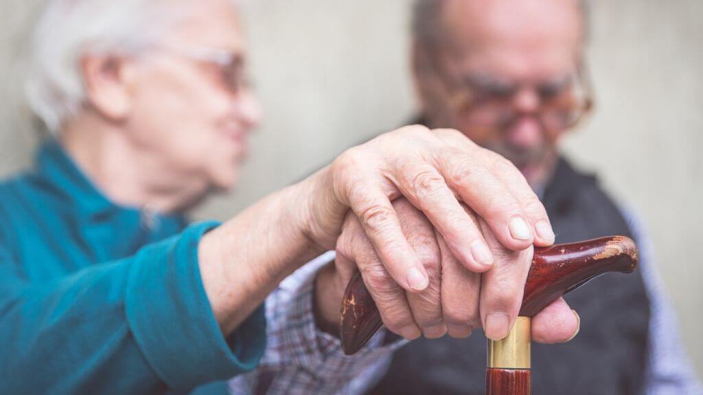 Older couple holdıng hands over a walking stick