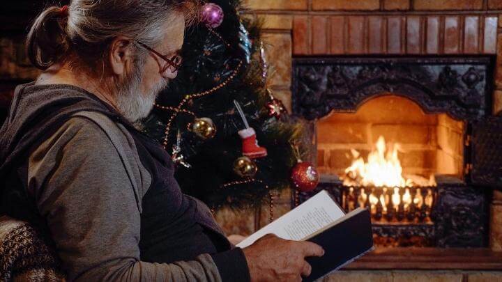 Man relaxing while reading a book by the fire on Christmas eve