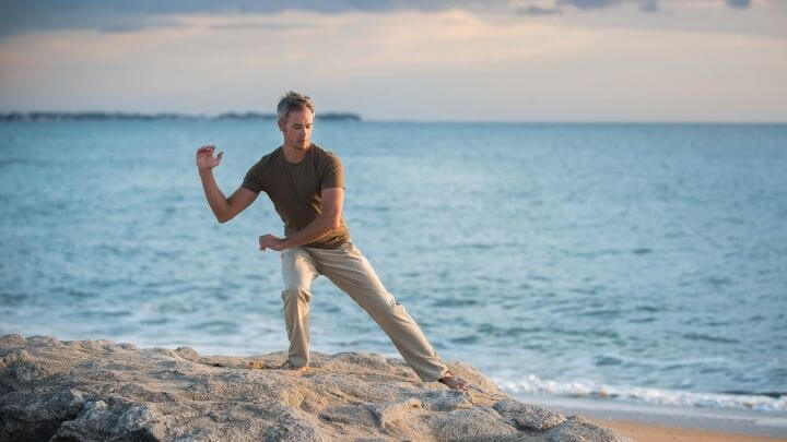 Man doing tai chi on a rock in the beach