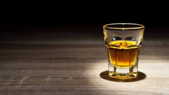 Whisky in a shot glass on wooden table