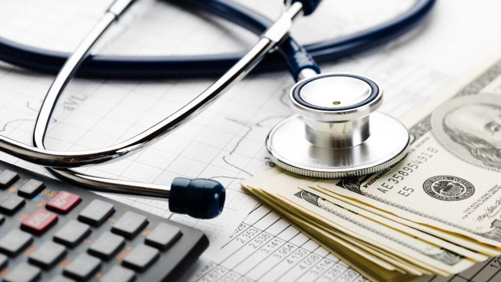 Hundred-dollar bills next to a stethoscope and a calculator, expensive healthcare concept