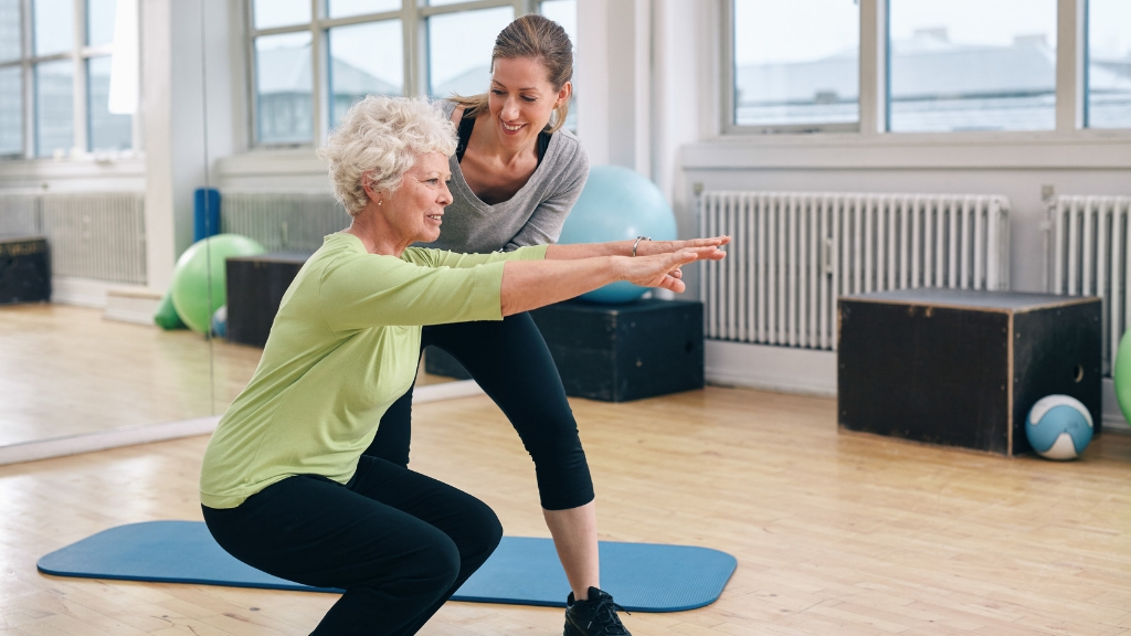 An older woman exercising with the assistance of a physical trainer