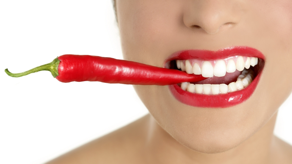 Woman holding hot red pepper between her teeth