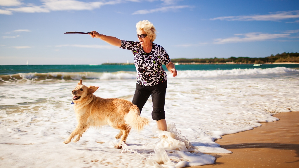 A senior woman playing with her dog in the beach