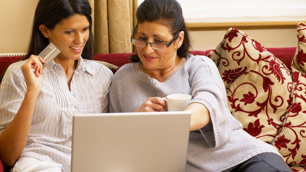a couple of women sitting on a couch looking at a laptop