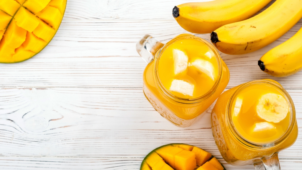 a glass of yellow liquid next to a bowl of fruit