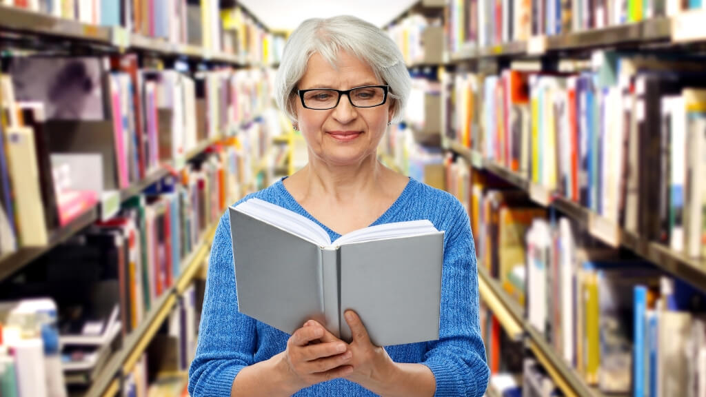 Smiling woman standing in a library isle reading a book.