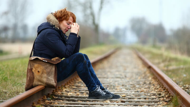 A middle aged woman crying while sitting on the railroad tracks