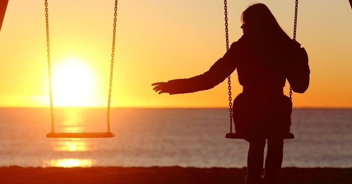 A woman sitting on a swing next to an empty one at sunset 
