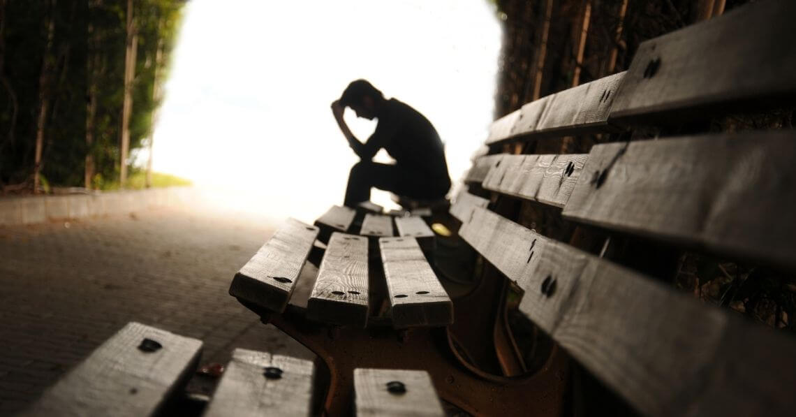 Silhouette of a sad man sitting at a bench