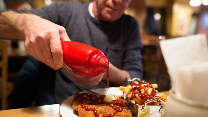 A man pouring ketchup on fried food