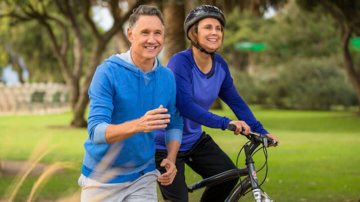 A middle aged man running while his wife is riding on her bike