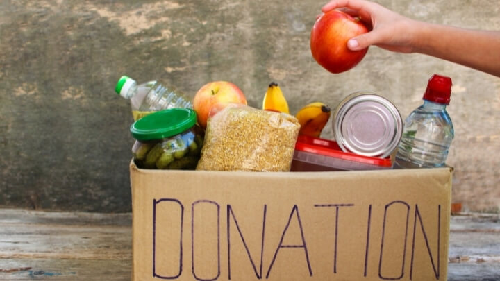 A woman putting an apple in a box marked for donation