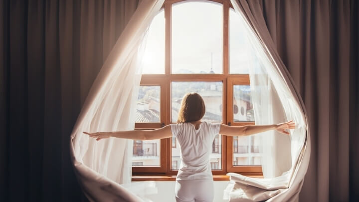 Woman opening the curtains after a night restful sleep