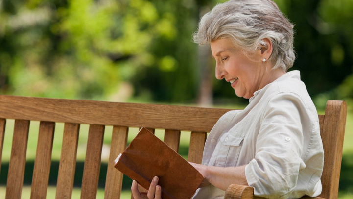 A senior woman reading her book on a park bench