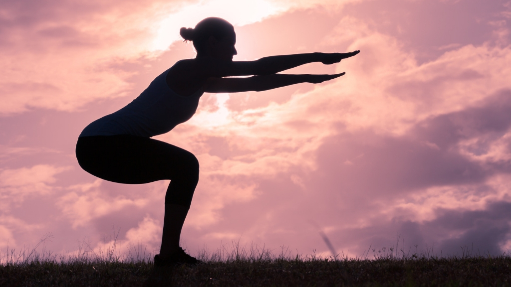 Silhouette of a woman doing squat exercises against the sunset.