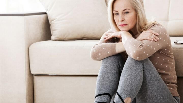 Sad woman sitting on the floor by the couch