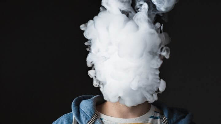 A vaping man with smoke covering his face