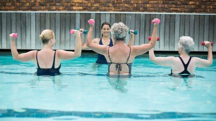 A group of senior women strenth train in the pool with an instructor