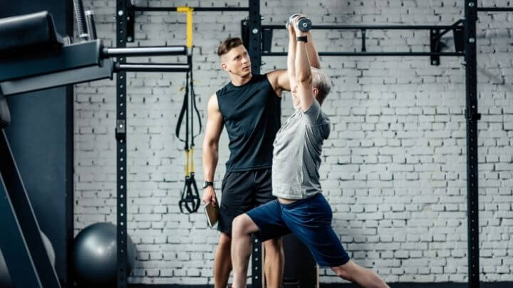 A middle-aged man works out at the gym with a trainer