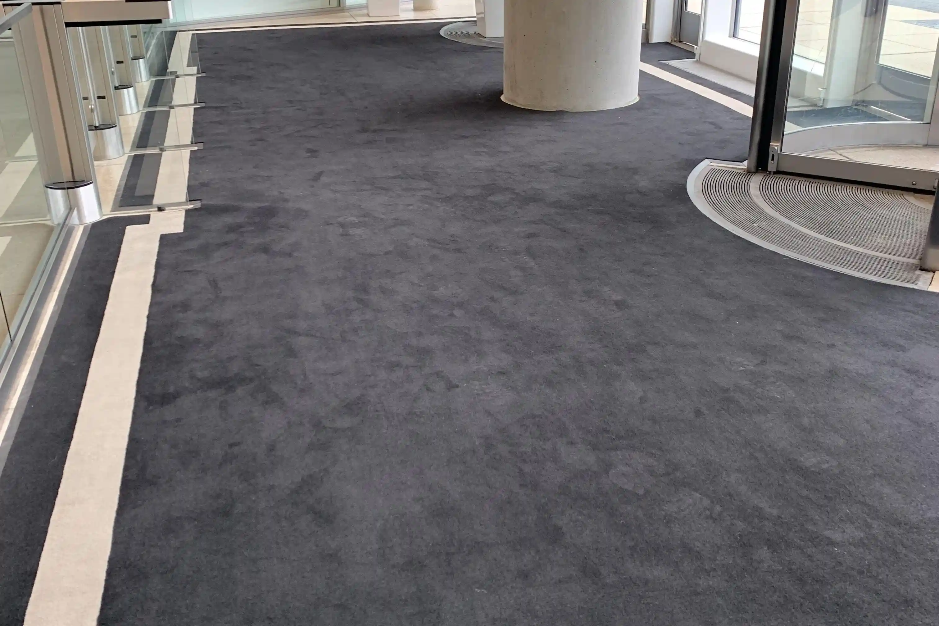 Matting by Design custom charcoal entrance mat fitted around a revolving door and pillars.