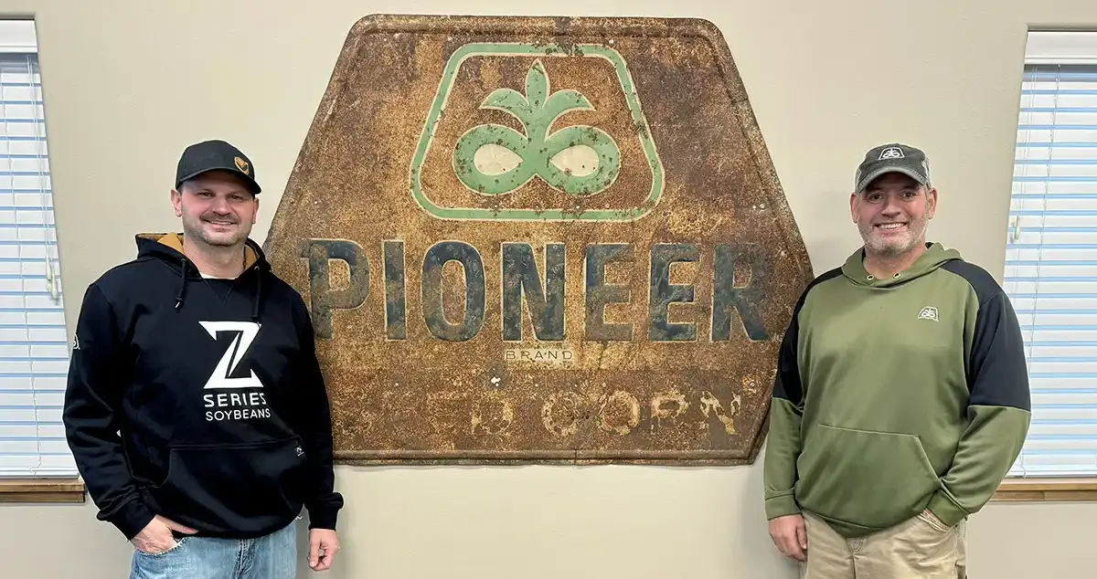 Two men standing in front of a large vintage Pioneer seed sign inside an office.