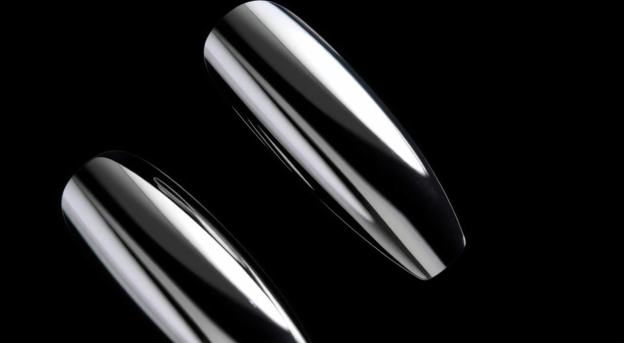 A close-up photograph of metallic chrome nails against a seamless black background, with dramatic side lighting that creates striking reflections and shadows. The nails have a mirror-like finish, with a sleek and futuristic appearance. The image captures the nails at a slight angle, emphasizing their curvature and the interplay of light and dark tones. The overall mood is modern, minimal, and sophisticated, highlighting the bold and eye-catching nature of the chrome nail trend.