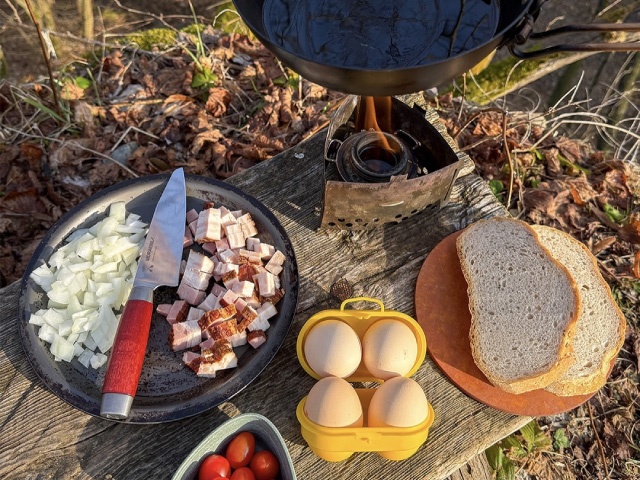 Slanina, cibule, vejce a pánvička připravené na vaření venku nad plotnou na líh