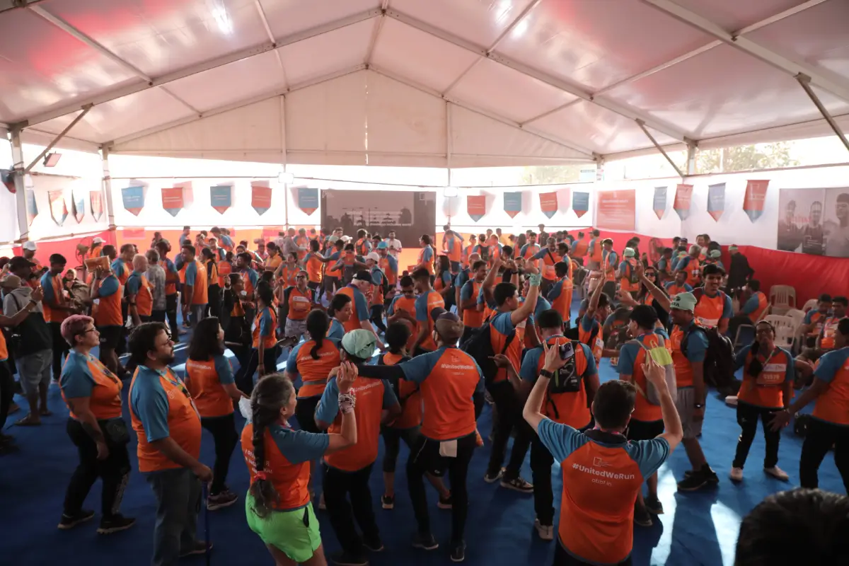 A large tent full of runners in orange and blue ABBF jerseys dancing and celebrating after a race.
