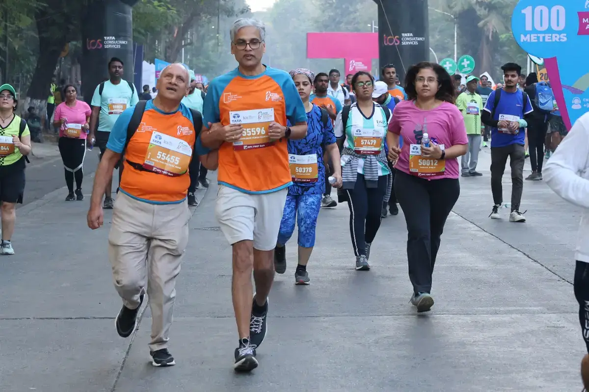 Two men in ABBF jerseys run arm in arm through a city marathon, other runners around them.