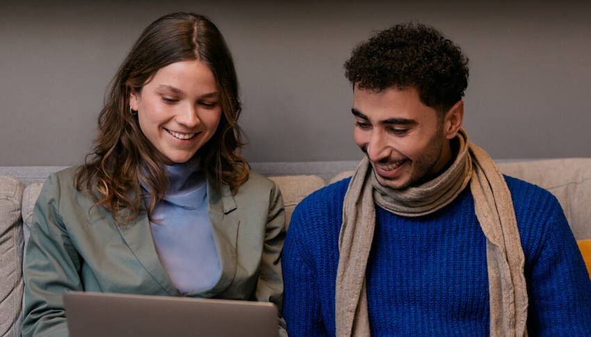 A man and woman seated on a sofa, engrossed in their work on a laptop computer.